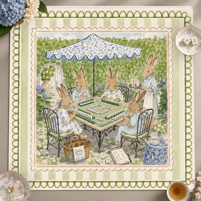 May include: A square fabric mat featuring a watercolor illustration of four rabbits playing mahjong under a blue and white umbrella in a garden. The border has a green scalloped pattern on a light green striped background with floral accents.
