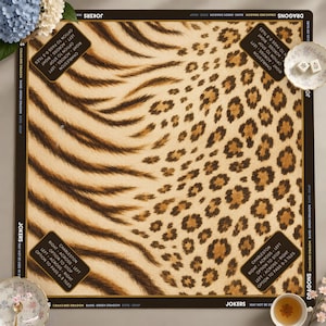 Op de afbeelding: Een vierkante Mahjong-mat met een centraal dierenprintpatroon met tijgerstrepen aan de linkerkant en luipaardvlekken aan de rechterkant. De zwarte rand bevat witte tekst met spelregels, Charleston-instructies en de namen van de stenen.