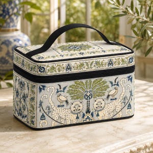 May include: A rectangular vanity case with a black handle and zipper closure. The exterior features a light blue background with a repeating pattern of two leopards, birds, and a central palm tree, accented by green and blue floral borders.