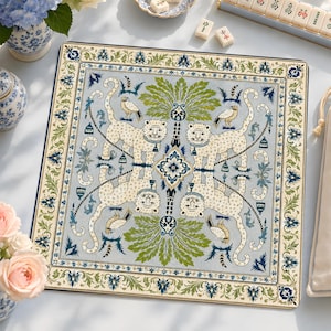 May include: A square mat featuring a symmetrical pattern of four cream-colored tigers with blue collars, green palm fronds, and small birds on a light blue background. The border displays a detailed green and blue floral vine motif.