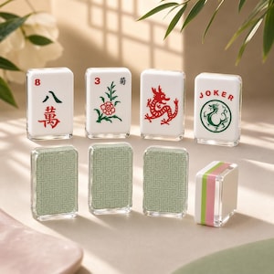 May include: A set of rectangular Mahjong tiles with white faces featuring red and green printed designs, including Chinese characters, a flower, a dragon, and the word JOKER. The reverse sides have a light green geometric pattern.