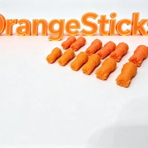 Peut inclure: Un ensemble de douze petits bâtonnets orange texturés disposés en groupe. Au-dessus des bâtonnets, le texte "OrangeSticks" est affiché en grandes lettres orange en trois dimensions avec un contour jaune sur un fond blanc uni.