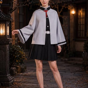 May include: A light grey cape with black trim and a red cord closure worn over a black collared shirt with white buttons, a black pleated skirt, a white belt with a silver buckle, and black ankle boots with side zips.