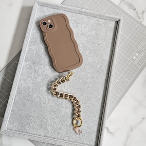 May include: A brown silicone phone case with a wavy design and a gold chain phone strap with a small charm.