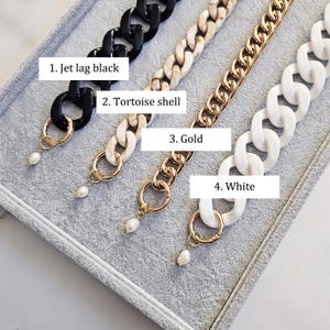 May include: Four chain-style necklaces in black, tortoise shell, gold, and white. Each chain has a different design and is attached to a gold-colored ring with a small, white pearl pendant. The text on the image reads: 1. Jet lag black, 2. Tortoise shell, 3. Gold, 4. White.