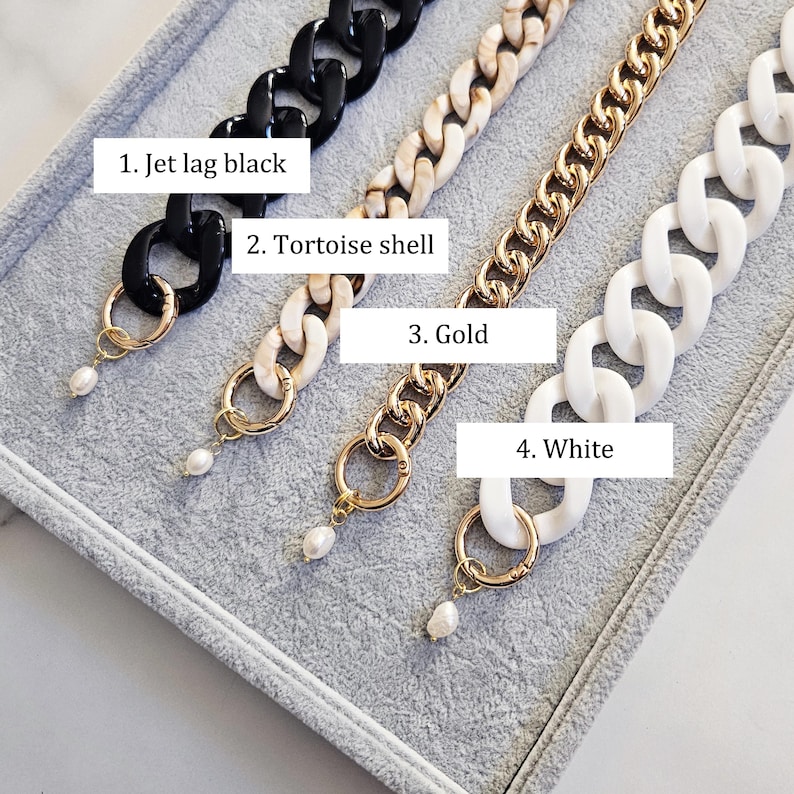 May include: Four chain-style necklaces in black, tortoise shell, gold, and white. Each chain has a different design and is attached to a gold-colored ring with a small, white pearl pendant. The text on the image reads: 1. Jet lag black, 2. Tortoise shell, 3. Gold, 4. White.