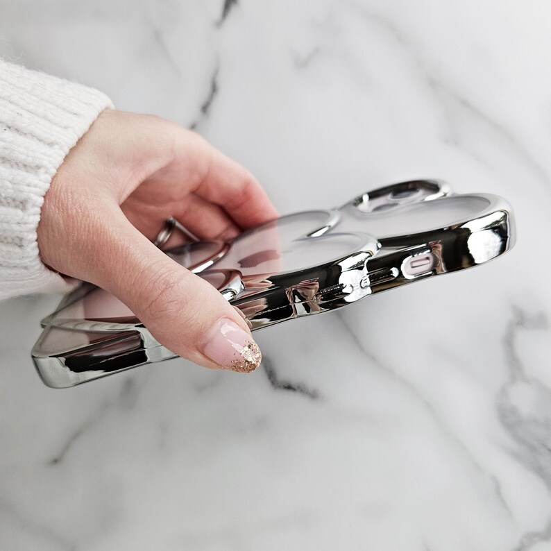 Op de afbeelding: Een zilveren telefoonhoesje met een transparante achterkant en een reli&euml;fdesign van twee harten. Het hoesje is gemaakt van duurzaam materiaal en heeft een strakke, moderne uitstraling.