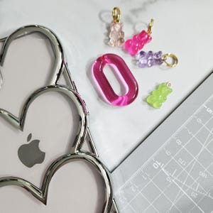 Op de afbeelding: Een set van vijf kleurrijke gummy bear bedels, waaronder roze, paars, groen en helder. De bedels zijn bevestigd aan gouden springringen en zijn perfect om een speelse touch toe te voegen aan sieraden of sleutelhangers.