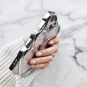 Op de afbeelding: Een zilveren telefoonhoesje met een transparante achterkant en een reli&euml;f hartontwerp. Het hoesje is gemaakt van duurzaam materiaal en heeft een strakke, moderne uitstraling.