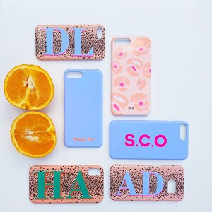 May include: Assortment of phone cases with various designs and personalized initials. The cases feature a pink and black spotted pattern with white lettering. The initials include "DL", "MOB", "S.C.O", "HA", and "AD".