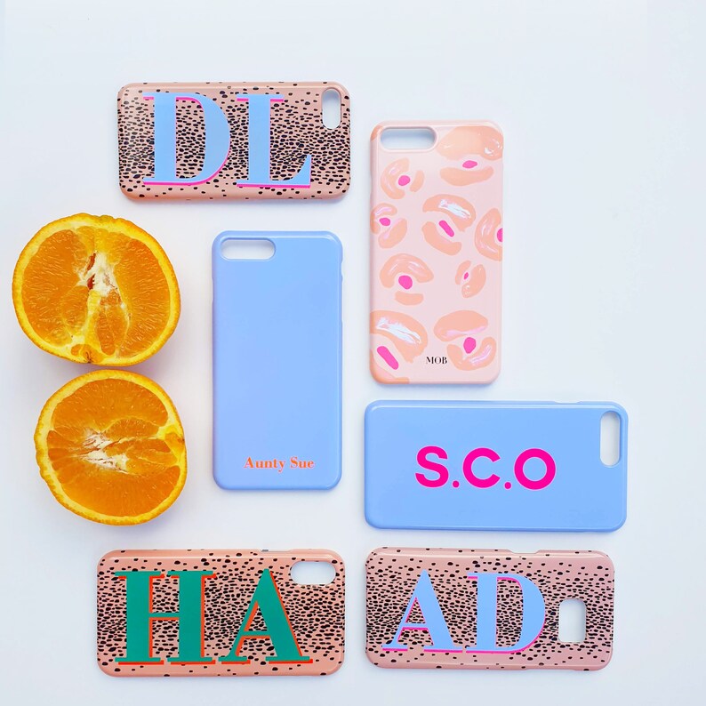 May include: Assortment of phone cases with various designs and personalized initials. The cases feature a pink and black spotted pattern with white lettering. The initials include "DL", "MOB", "S.C.O", "HA", and "AD".