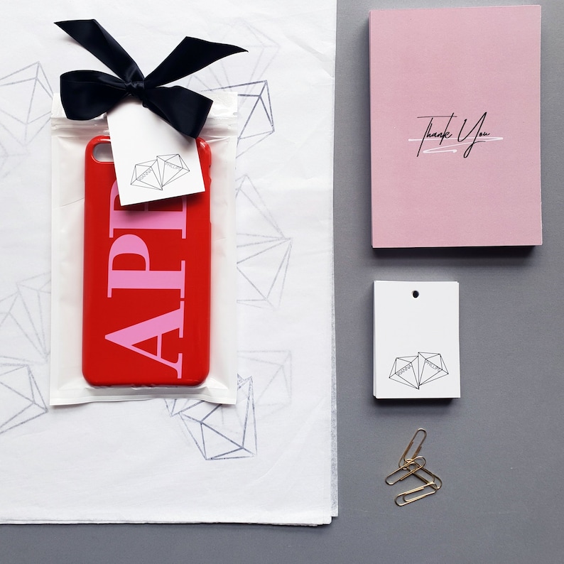 May include: A red phone case with a pink "API" design, a thank you card, and a small white tag with a geometric design. The items are on a white background with a geometric pattern.