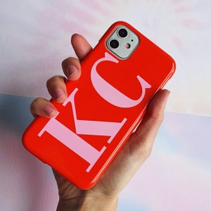 Puede incluir: Una funda de teléfono roja brillante con las letras "KC" en rosa.