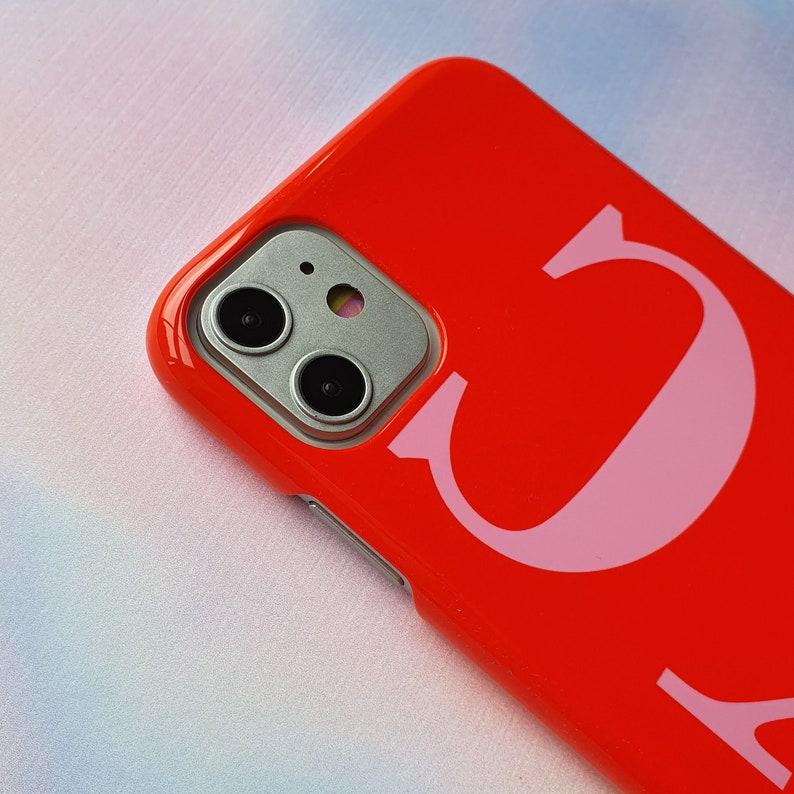 May include: A bright red phone case with a pink letter "C" printed on the back. The case has a camera lens cutout.