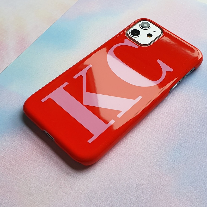 May include: A red phone case with the letters "KC" in pink on the back.