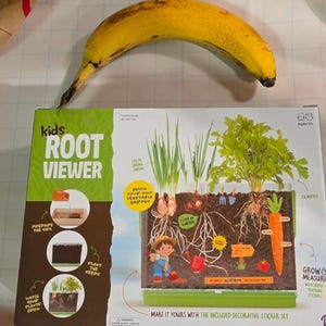 May include: A Kids Root Viewer gardening kit box featuring illustrations of spring onions, cilantro, and a carrot growing in soil. The packaging includes text such as Grow Your Own Vegetable Garden, Grow & Measure, and instructions for planting seeds.
