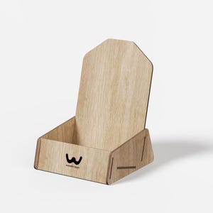 Peut inclure: Un présentoir en bois brun clair avec un panneau arrière haut et un plateau avant bas. Le panneau avant présente un logo noir avec le texte "woodin laser" imprimé en dessous. La structure est assemblée avec des joints visibles.