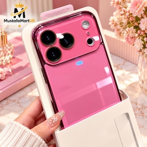 May include: A bright pink smartphone case featuring a glossy finish, a triple camera cutout with dark circular lenses, and a small rectangular light indicator. The case is presented in a white packaging sleeve with the MustafaMartUK logo.