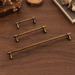 May include: Three metal drawer pulls in a dark antique brass finish, each featuring a long, slender horizontal bar supported by two small, flared conical posts at either end. The pulls are arranged in a diagonal line from smallest to largest.