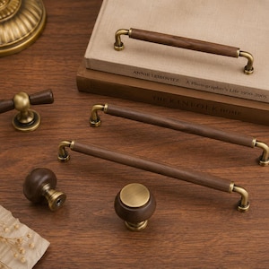 May include: A collection of cabinet hardware including three long bar pulls with dark brown wooden centres and antique brass metal ends, two round wooden knobs with brass bases, and one T-shaped wooden handle with a brass centre post.