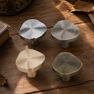 May include: Four cabinet knobs with an irregular, rounded shape and a concentric spiral pattern on the top surface. The set includes one polished chrome, one brushed nickel, one brushed gold, and one antique bronze finish knob.