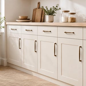 May include: Off-white kitchen cabinets featuring shaker-style doors and drawers with dark bronze metal hardware pulls. The cabinets are topped with a light wood countertop, creating a clean and functional storage space for a kitchen area.