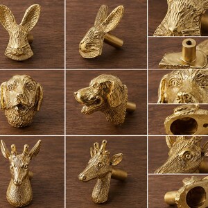Puede incluir: Una colecci&oacute;n de tres pomos para armarios de metal en tono dorado con forma de cabezas de animales. La fila A muestra un conejo, la fila B un perro y la fila C una jirafa. Cada pomo incluye un poste de montaje cil&iacute;ndrico en la parte trasera.