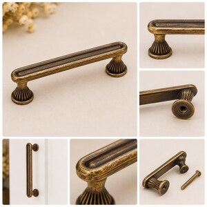 May include: A bronze-toned metal cabinet pull with a rectangular bar and two fluted, pedestal-style bases. The handle features a recessed center channel and a distressed finish. It is shown from multiple angles, including a view with a mounting screw.