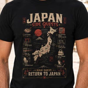 May include: A black t-shirt featuring a graphic print titled Japan Side Quests. The design includes a map of Japan, Mount Fuji, and a checklist of activities like eating ramen, visiting a shrine, and using a Japanese toilet, with the text Main Quest: Return to Japan at the bottom.