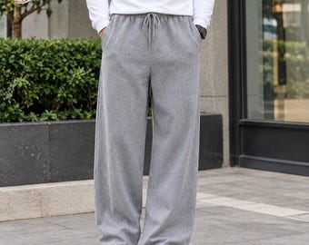 May include: A pair of heather gray sweatpants featuring a wide-leg silhouette, an elastic waistband with a drawstring closure, and two side pockets. The sweatpants are paired with a long-sleeved white shirt and white athletic sneakers.