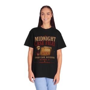 May include: A black t-shirt featuring a graphic with the text MIDNIGHT CASE FILES, COLD CASE DIVISION, OCTOBER 31, and @TRUECRIMESTORY011. The design includes a brown file folder labeled OPEN, a moon, and a jack-o'-lantern illustration.
