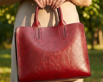 May include: A structured rectangular handbag in a deep burgundy red color with a smooth, slightly glossy finish. The bag features two sturdy top handles attached with reinforced stitching and a clean, minimalist design with no external pockets.