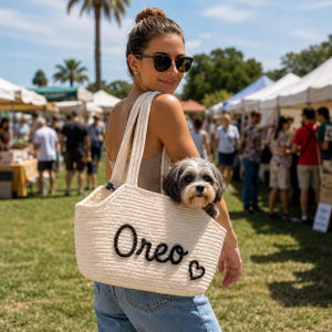 May include: A cream-colored rope pet carrier bag featuring the name Oreo and a small heart shape in black yarn lettering on the front. The bag has two long shoulder straps and is designed to carry a small dog inside the open top compartment.