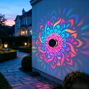 May include: A circular solar-powered wall light mounted on a white exterior wall, projecting a vibrant, multi-colored mandala-style light pattern in shades of pink, blue, and orange onto the surface during the twilight hours.