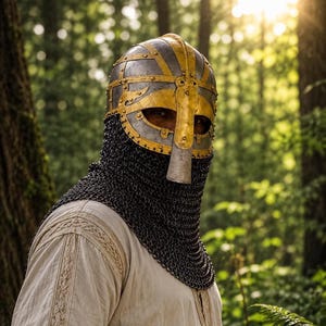 May include: A metal helmet featuring a gold-coloured nasal guard and decorative bands over a dark chainmail coif. The helmet is constructed with riveted steel plates and a central vertical bar. It is worn over a light-coloured, textured tunic.