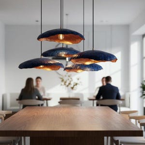 Può includere: Un gruppo di cinque lampade a sospensione fissate al soffitto, ciascuna caratterizzata da un paralume ampio e poco profondo di forma organica, con esterno blu scuro e interno in metallo dorato caldo, che ospita una lampadina visibile.