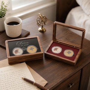 May include: Two rectangular wooden display boxes with hinged lids, each featuring the engraved name Oliver and the date 11.22.2026. The boxes contain two circular coins in protective capsules, with one box featuring a dark interior and one a red velvet lining.