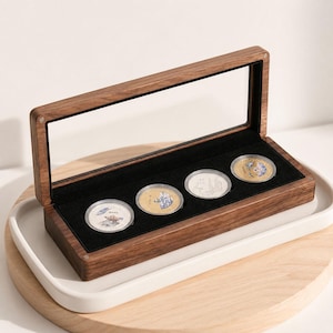 May include: A rectangular wooden display box with a clear hinged lid, featuring a black velvet interior lining. Four circular coins are arranged in a row within the case, each encased in a protective plastic capsule, showcasing varied designs.