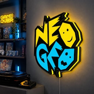 Puede incluir: Un letrero LED de pared con el texto NEO GEO en una fuente estilizada. La palabra NEO es de color amarillo brillante y la palabra GEO es de color azul claro. Dos iconos de caras circulares están integrados en el diseño, uno amarillo y otro azul.