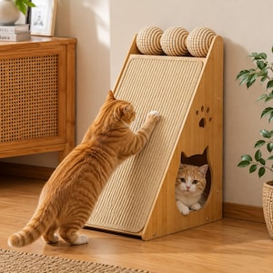 Peut inclure: Une rampe à griffer pour chat en bois clair avec une surface en sisal texturé, trois balles tressées au sommet et une découpe en forme de chat à la base. Un chat tigré orange se tient sur ses pattes arrière pour griffer, un autre est assis.