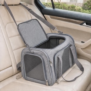 May include: A grey pet carrier with a rectangular structure, featuring mesh ventilation panels on the sides and front, a top-opening zippered flap, and an adjustable shoulder strap. The carrier is constructed from a textured fabric material.