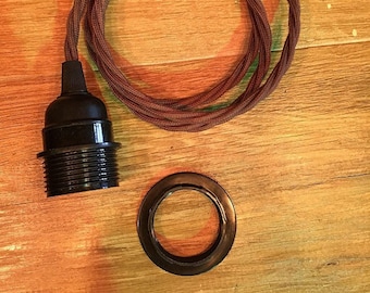 May include: A black light socket with a brown, twisted electrical cord and a matching black ring. The cord is coiled and secured with a black tie. The items are on a wooden surface.