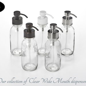 Peut inclure: Cinq flacons en verre transparent avec des pompes de couleurs différentes. Les flacons sont tous de la même taille et de la même forme. Les pompes sont noires, blanches et argentées. Les flacons sont sur une surface blanche. Notre collection de distributeurs à large ouverture transparents.