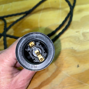 Op de afbeelding: Close-up van een zwarte lamphouder met goudkleurige metalen contacten. De lamphouder is gemarkeerd met "RS-1907A", "660W" en "250V". Een zwart, gevlochten elektrisch snoer is zichtbaar op de achtergrond. De lamphouder is gemarkeerd met "RUI CHENG" en "LISTED".