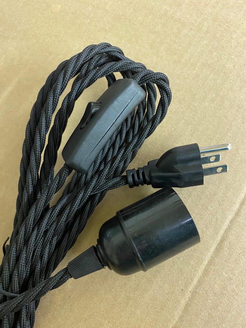 Op de afbeelding: Zwart gevlochten elektrische kabel met een zwarte in-line schakelaar, een zwarte stekker en een zwarte lamphouder. De kabel is strak geweven. Componenten zijn ontworpen voor elektrisch gebruik. Kabellengte: ongeveer 100 cm.