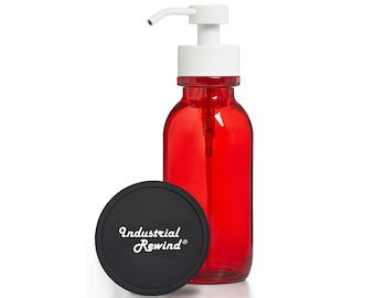 Puede incluir: Una botella de vidrio rojo con un dispensador de bomba blanco y una tapa negra. La tapa tiene el texto "Industrial Rewind" en una fuente cursiva. La botella es probablemente para jabón o loción.