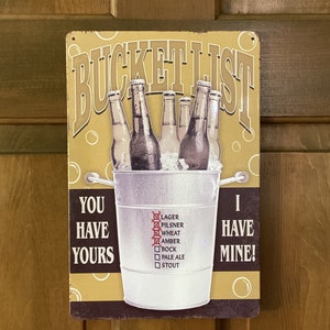 May include: A rectangular metal sign with the words "Bucket List" at the top. The sign features an illustration of beer bottles in a bucket of ice. The text "You Have Yours, I Have Mine!" is also present, along with a checklist of beer types.