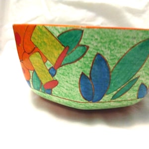 May include: A ceramic bowl featuring a vibrant hand-painted design with a textured light green background, accented by bold orange, blue, and dark green leaf-like shapes outlined in dark brown, with a solid orange rim along the top edge.