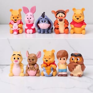 以下が含まれることがあります： くまのプーさんのキャラクターの小さなカラフルなフィギュア10体セット。プーさん、ピグレット、イーヨー、ティガー、ラビット、カンガ、ルー、クリストファー・ロビン、オウルが含まれており、白い表面に2列に並べられています。