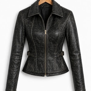 May include: A black jacket with a distressed, weathered texture, featuring a pointed collar, long sleeves, and a central gold-toned zipper closure. The garment includes side waist tabs with metal buckles and vertical seam detailing throughout.
